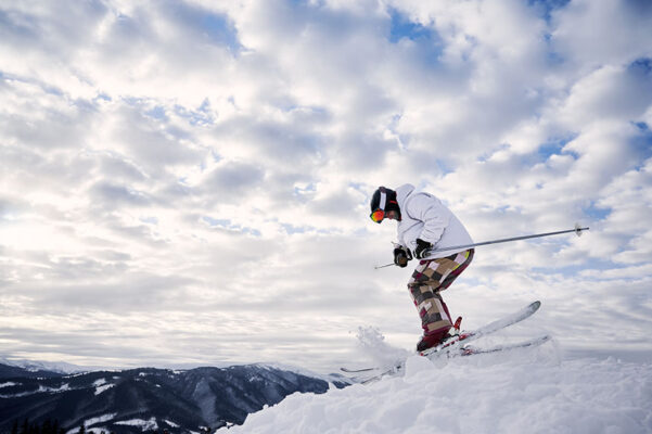 Side view of male skier in winter jacket sliding down snow covered slopes